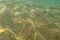 Underwater photo, sea bottom in shallow water, sun shining, light refracting on sand dunes. Abstract marine background