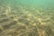 Underwater photo, sun shining on sea floor in shallow water, sand forming
