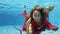 Underwater portrait of a cute young girl with long hair who dives and swims in a pool in a red dress, looks at the