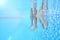 Underwater Shot Of Couples Legs As They Sit On Edge Of Swimming Pool On Vacation