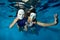 Underwater theater. Two unusual girls swim and play underwater in the pool on a blue background in white masquerade masks