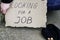 Unemployed man sitting on the ground holding the cardboard sign saying looking for a job next to is a hat with alms coins