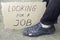 Unemployment concept man in old torn shoes sits on a ground at his feet cardboard sign saying looking for a job