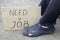 Unemployment concept man in old torn shoes sits on a ground at his feet cardboard sign saying need a job
