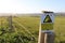 Unfenced Cliff with overhangs ahead post sign yellow and white with green field in the background.