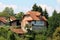 Unfinished red brick family house next to wooden garden tool shed surrounded with older houses and tall trees