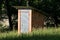 Unfinished small narrow homemade garden tool shed made from red building blocks and closed with metal doors locked with padlock