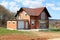 Unfinished under construction small suburban red brick family house with attached garage surrounded with grass and tall trees with