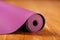 An unfolded lilac-colored yoga mat is unfolded on the wooden floor.
