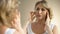 Unhappy aged woman looking in mirror at home, touching her face, aging process