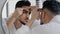 Unhappy arabian indian arab bearded man looking in bathroom mirror feeling worried about facial skin problem acne