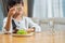 Unhappy Asian little young girl child don`t want to eat green vegetables on dinner plate. Small kid daughter smelling on cucumber