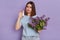 Unhappy attractive sick woman suffers from runny nose showing nasal spray for treating allergic rhinitis reaction on flowers,