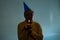 Unhappy birthday guy in yellow t-shirt and blue cap standing on white background holding birthday cake making a wish.