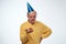 Unhappy birthday guy in yellow t-shirt and blue cap standing on white background holding birthday cake making a wish.