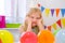 Unhappy blonde caucasian girl with boring face near birthday rainbow cake. Festive colorful background. Bad birthday