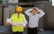 Unhappy customer in stress and constructor foreman worker with helmet and vest arguing outdoors on new house building blueprints