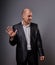 Unhappy depressed bald busuness man in black suit showing the palm stop sign on grey background. Closeup