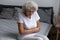 Unhappy elderly woman sitting on bed, feeling strong belly ache