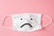 Unhappy face on Protective white face mask on pink background..