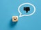 Unhappy face on a wooden cube with a dislike thumb down gesture icon in a speech bubble