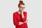 Unhappy ginger teenager has sleepy dejected facial expression, ginger knot, keeps hand under chin, dressed in casual red sweater,