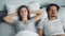 Unhappy girl covering ears with pillow while husband snoring in bed