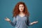 Unhappy good-looking girl with ginger wavy hair and freckles looking in camera, spreading hands with angry and annoyed