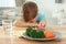 Unhappy little boy refusing to eat vegetables at table