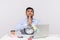 Unhappy man employee sitting in office workplace, holding clock looking imploring with prayer gesture, begging