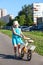 Unhappy preschool girl carrying her bicycle on asphalt lane holding steering wheel