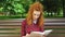 Unhappy red haired girl reading thriller in park