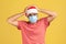 Unhappy sad man in red t-shirt and santa claus hat with surgical medical mask on face touching head, migraine, fear of contracting