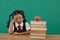 Unhappy schoolgirl looking at books stack and apple against chalkboard