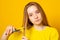 Unhappy teen girl cutting her hair with scissors while standing yellow background. Young student experiments with her hairstyle