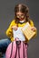 Unhappy tired schoolgirl in eyeglasses puting the exercise books in pink backpack on grey studio background in fashion style