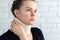 Unhappy woman with cervical surgical collar feeling pain in neck against a blurred white brick wall background