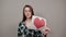 Unhappy woman with glasses holds piece of paper with red heart in hand