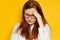 Unhappy young woman with red long hair and glasses suffers a headache, migraine on a yellow wall background. Stress