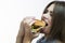 Unhealthy Eating Concepts. Closeup of Caucasian Woman Eating Burger. Profile Face View. Posing in Striped Shirt Indoors in Studio