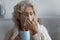 Unhealthy elderly woman blowing runny nose drinks antiviral beverage