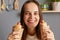Unhealthy food. Brown haired Caucasian young adult positive woman holding two hot dogs feels hungry, looking smiling at camera,