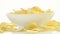 Unhealthy Harmful food, yellow delicious Potato ribbed crispy chips randomly lying in bowl and on a white table background, close-