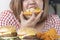 Unhealthy junk food concept. Hands of oversize fat woman eating pizza with hamburger and chicken fried on table. Close up