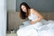 Unhealthy young woman sitting on bed and holding belly, feeling discomfort and suffering from stomachache, food poisoning, on