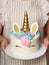 Unicorn cake with a golden horn and colored mane in the hands of a girl. Cream cake with meringues