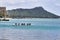 Unidentifiable men rowing out to sea on an outrigger with Diamond Head in the distance.