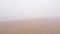 Unidentifiable person walking on the beach in foggy weather