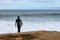 An unidentifiable woman in a wetsuit holiding her surfboard waiting for the right time to join the surf, coastal Victoria, great