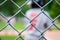 Unidentifiable youth junior league baseball player in team uniform, seen from behind through wire fence